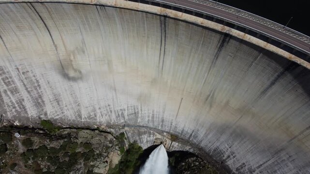 4K aerial drone video advancing and tilting down to capture the massive concave concrete wall of the Almendra Dam in Salamanca, Spain. The impressive shot highlights the immense engineering structure