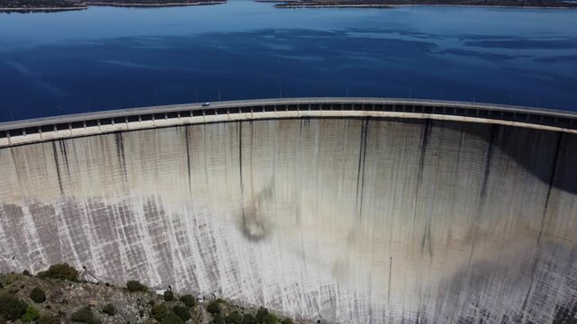 4K aerial drone video featuring a wide general shot of the massive front face of the Almendra Dam in Salamanca, Spain. The impressive footage captures the immense curved concrete wall, high-pressure w