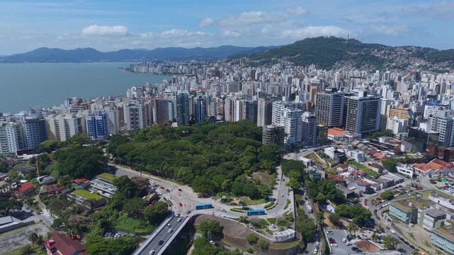 Drone flyover of downtown Florianopolis Brazil on a clear sunny day showcasing the city skyline dense urban buildings coastline and surrounding green mountains