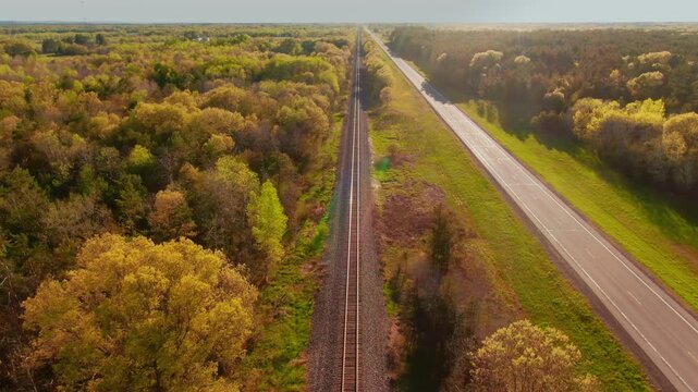 Railroad tracks run parallel to a quiet highway through a colorful lush forest in Wisconsin. Ideal for transportation or travel-themed projects.