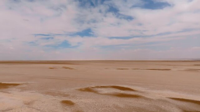 Aerial drone shot over the dry Chott el Djerid salt lake. Cinematic perspective of the vast crystalline salt flats under a cloudy sky in southern Tunisia, North Africa