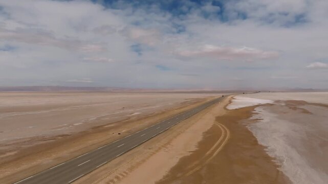 Aerial drone view of the lonely asphalt road crossing the Chott el Djerid salt lake. Scenic desert landscape with white salt flats and cloudy sky in southern Tunisia, North Africa