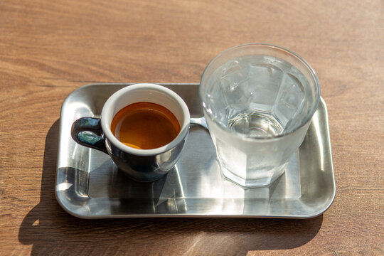 Espresso shot in ceramic cup served with iced water on metal tray overhead view.