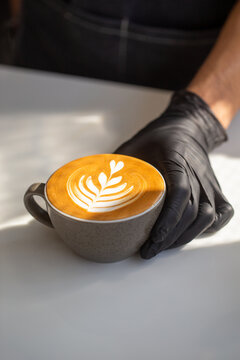 Barista holding a cup of hot latte art with leaf pattern close-up.