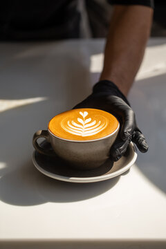 Professional barista serving hot cappuccino with latte art on saucer.