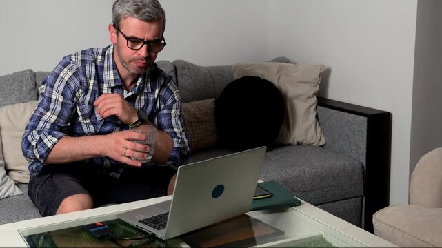 Freelancer working at home on a laptop in a cozy room while taking a break with a drink