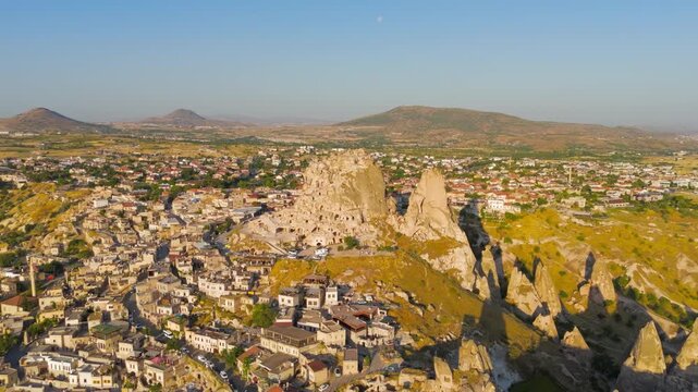 Uchisar, Nevsehir, Turkey. Uchisar Castle, a 60-meter volcanic tuff rock fortress honeycombed with ancient cave dwellings, aerial view in bright morning sun over the Cappadocia landscape. Aerial View