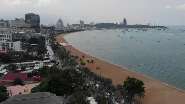 Pattaya Crescent Bay and Cityscape Aerial View - Standard Color. Wide drone panoramic shot flying over the crescent-shaped Pattaya beach and tropical bay, revealing coastal hotels, skyscrapers, and nu
