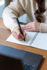 Vertical closeup image of a woman writing on a notebook while working on laptop computer at home