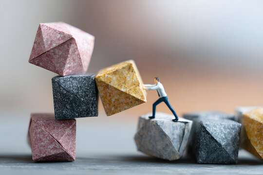 Leader stabilizing a tower of origami cubes representing risks, team supporting the structure, balancing strategy theme