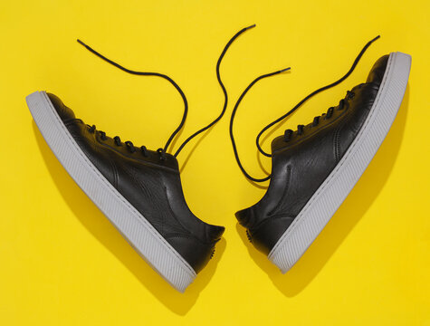 Black leather classic men's sneakers with light sole, yellow background. Top view