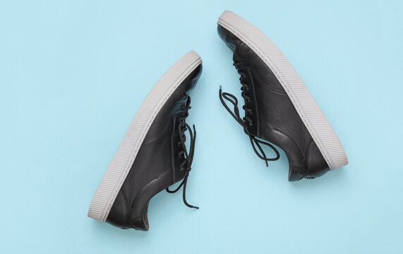 Black leather classic men's sneakers with light sole, blue background. Top view
