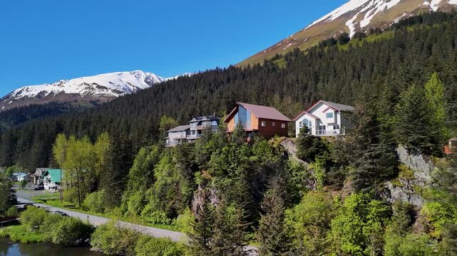 Seward, Alaska downtown sits near the shoreline bay area under a clear blue sky in summer. Boats, buildings, and mountains create a scenic coastal view. Perfect stock footage for travel, tourism, city
