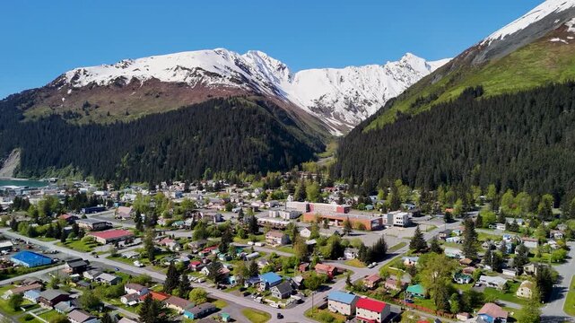 Seward, Alaska downtown sits near the shoreline bay area under a clear blue sky in summer. Boats, buildings, and mountains create a scenic coastal view. Perfect stock footage for travel, tourism, city
