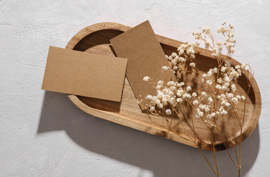 Craft blank business cards mockups with dry grass in tray on white concrete background