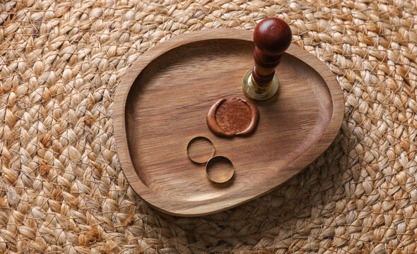 Gold rings and vintage sealing wax stamp in a wooden tray on a woven straw mat. Wedding planning concept