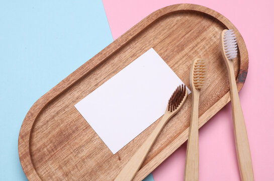 Wooden toothbrushes with white blank business card in wooden tray on pink blue background. Oral care concept. Top view