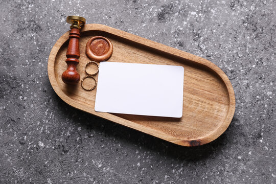 Gold rings, vintage stamp in a wooden tray and blank business card on dark concrete background