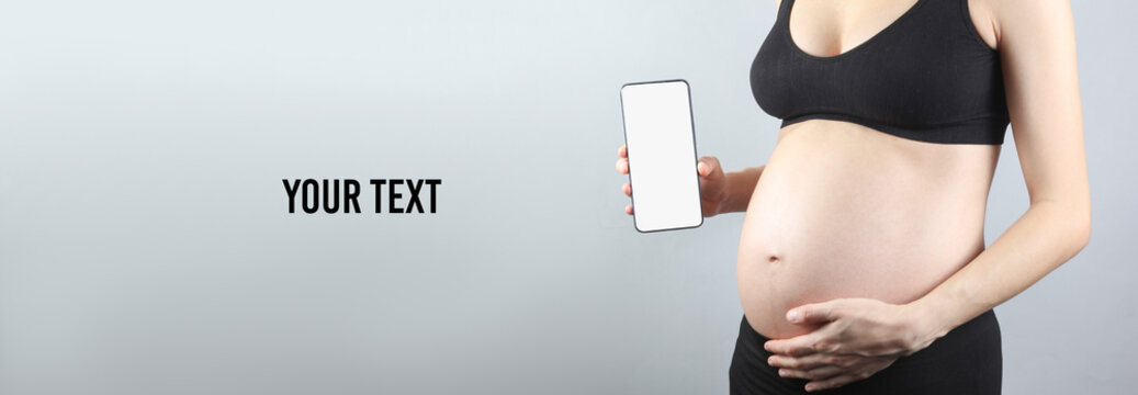 Pregnant woman holding smartphone with a white blank screen on a gray background. Mockup, design template, your information. Copy space for your text