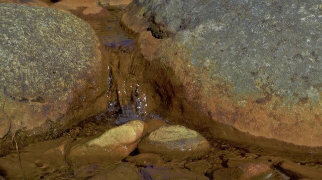 Stream, brook flows down through mountain rocks with a red coloration caused by minerals in the water and algae. The formation can resemble female legs, and the vagina has a constant peeing motion.