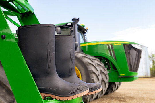 Spirit River, Alberta, Canada - May 17, 2026: agricultural machinery Green and yellow John Deere equipment in the farm yard on the background of blue sky and black rubber boots on the steps.