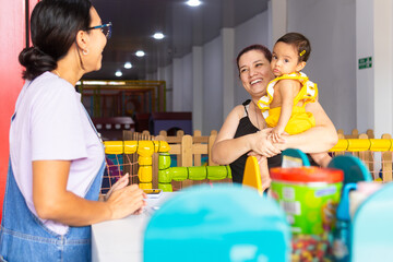 Two adult women and a baby sharing a welcoming moment at a childcare center, reflecting trust, care...