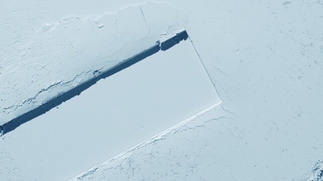 From-above capture of a pale blue flat powder surface with a dragged rectangular trace lit by dynamic orbiting light that projects moving shadows