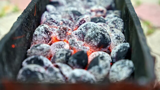 Side view of glowing hot charcoal in metal brazier for home barbecue cooking. Close up outdoor grilling scene with red embers, ash covered coals and heat.