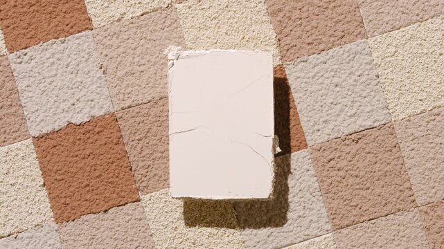 Top view shot of a beige pressed powder rectangle casting a dynamic shadow over a background of sifted powder mosaic in skin tone shades | Abstract pressed powder concept