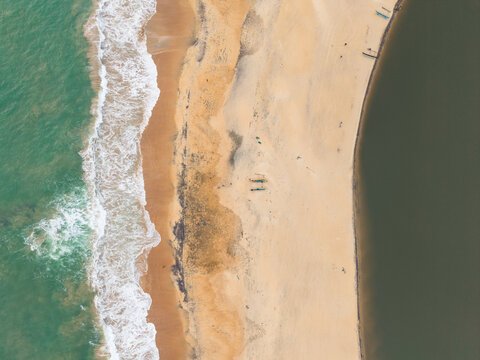 Aerial view of a sandy beach strip separating turquoise ocean waves from a calm dark lagoon with small fishing boats Galle, Southern Province, Sri Lanka.