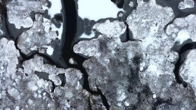 Aerial view of a frozen lake with ice patterns and dark water channels