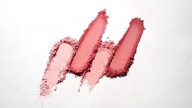 From-above shot of four red colored long powder smears on a light grey backdrop lit with dynamic orbiting light that projects moving shadows | Commercial idea for blush