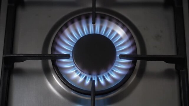 Gas stove burner ignition sequence on stainless steel cooktop. Blue flames lighting up in circular motion. Modern kitchen appliance for home cooking and culinary preparation.