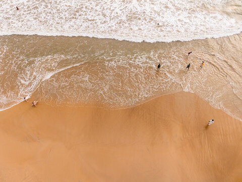 Aerial view of people relaxing and walking on a golden sandy beach with gentle ocean waves washing ashore in Galle, Southern Province, Sri Lanka.