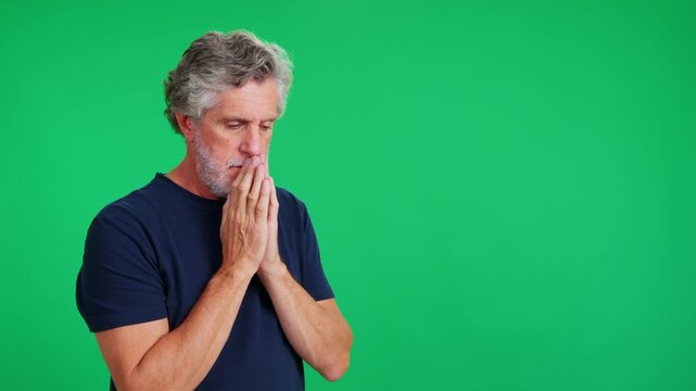 Mature man with grey hair praying on a green screen background