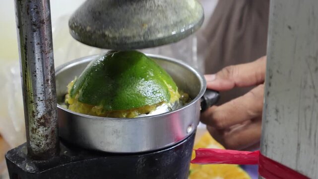 A close up of a vintage mechanical manual press machine squeezing a green citrus orange to make fresh juice.
