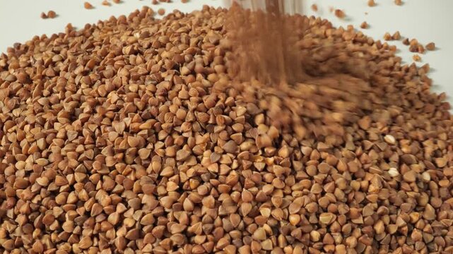 Raw buckwheat groats pouring onto a white plate