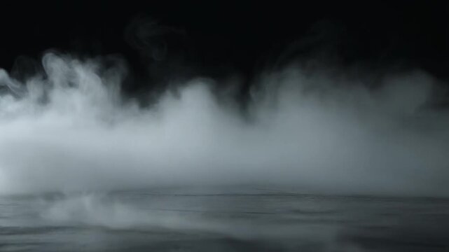 White smoke rolling over a dark textured surface. Cinematic thick fog wafting across a black background. Atmospheric steam effect for movie trailers or mysterious scenes.