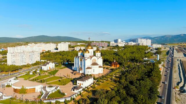 Gelendzhik, Russia. Cathedral of St. Andrew the First-Called, its five golden domes and white stone facade rising above the M4-Don Highway, aerial drone view under clear morning sky. Drone footage