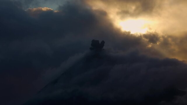 Active volcano spewing ash and smoke into a dramatic sky with glowing clouds during a sunset