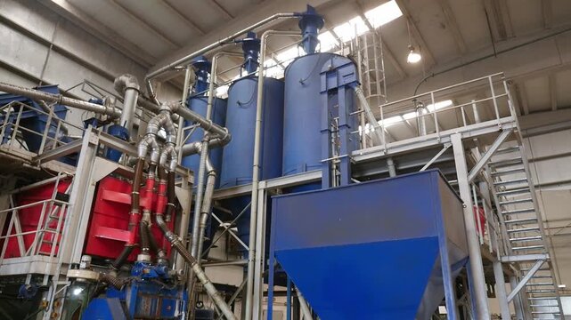 Pan left shot inside a modern waste tire recycling facility showing large blue processing silos, complex industrial pipes, and white steam exhaust from the machinery.