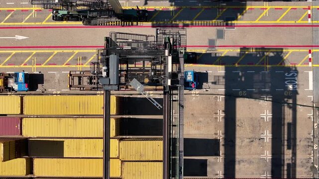 Aerial view of a container terminal showing trucks transporting cargo. Crane systems load and unload shipping containers. Visible organization of the loading and unloading process at a busy port.