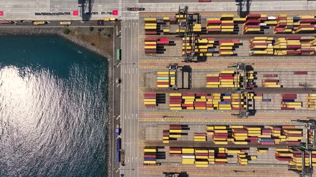 Container ships wait at the port due to shipping congestion. Cargo is stacked on docks, showing delays in freight transportation. Port operations continue despite challenges.