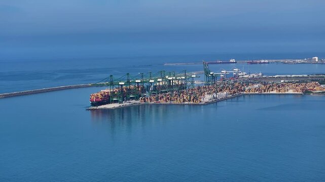 View of a busy port with multiple ships docked. Cranes are in operation for loading and unloading cargo containers. Shipping congestion affects international trade and logistics.
