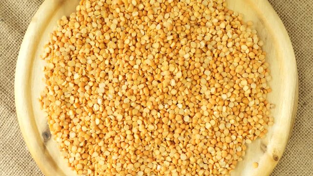 Yellow split peas rotating on a wooden plate
