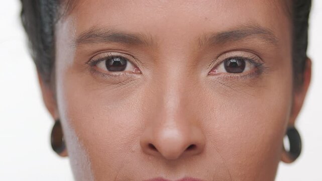 Extreme close-up of latin woman light brown complexion opening her eyes focusing on matte skin against white background | Face care advertisement