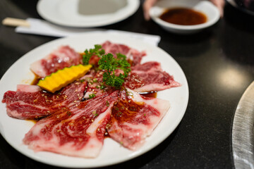 Obraz premium Premium raw Wagyu beef slices with beautiful marbling, marinated in soy sauce, served on a white plate with pumpkin. High-quality Japanese Yakiniku BBQ meat in a restaurant dining atmosphere.