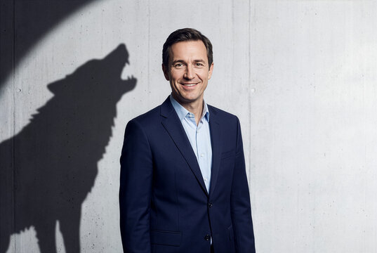 Friendly businessman casting a fierce howling wolf shadow on a concrete wall