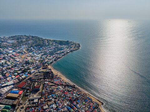Aerial view of dense urban sprawl along the coastline with colorful rooftops and the sun reflecting on the Atlantic Ocean Monrovia, Montserrado, Liberia.