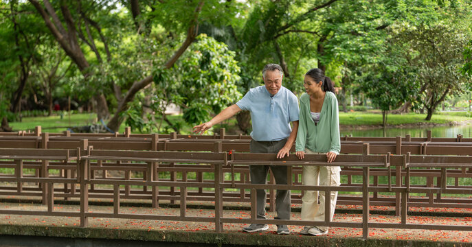 Smiling senior man and young woman having romance love conversation dating outdoors in greenery nature. Happiness age gap couple enjoying date relationship and talking together in public park.